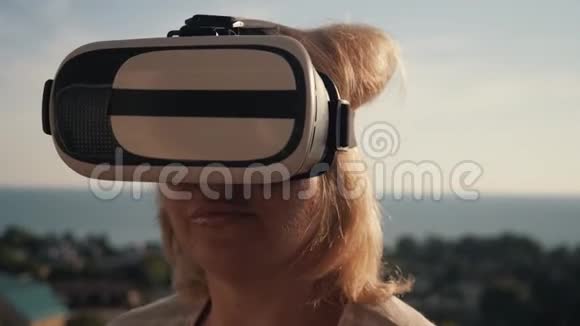 太阳落山时一个戴着虚拟现实眼镜的女孩在房子的屋顶上生命生命概念视频的预览图