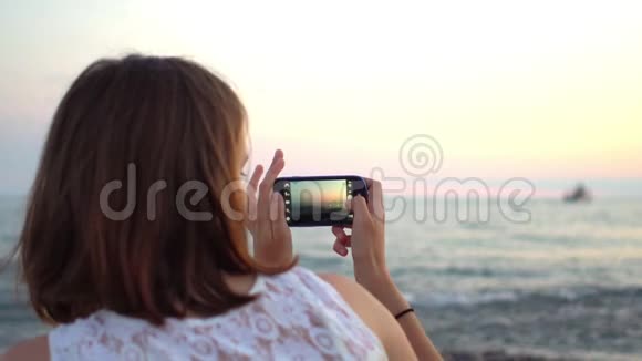 年轻潮女在海滩上用智能手机拍照视频的预览图