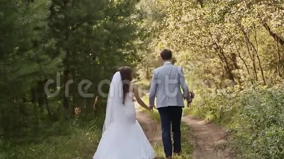 新娘穿着白色礼服在森林里新郎他们牵着手一起走一起快乐结婚纪念日视频的预览图