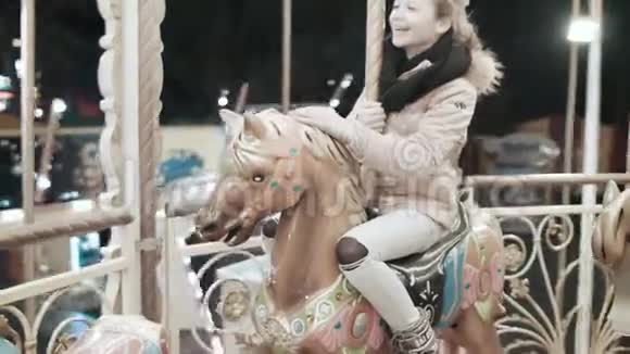 快乐的女孩骑着旋转木马坐在马上游乐园里的一个年轻女孩视频的预览图