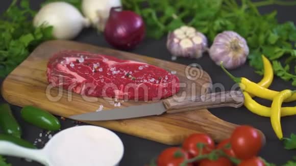 生的一块美味的牛排加盐在木板上放胡椒在黑桌上放蔬菜视频的预览图