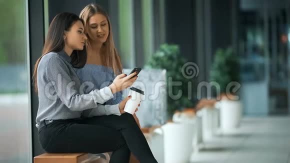 两个有魅力的年轻女人拿着购物袋一起看着手机视频的预览图