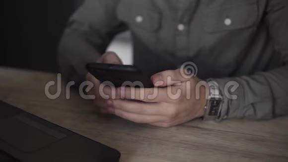 年轻的商人或学生穿着衬衫坐在笔记本电脑上用智能手机与他的商业伙伴一起使用视频的预览图