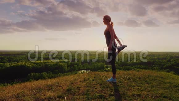 年轻女子在日落时在一个史诗般美丽的地方做伸展运动从阳光下看出来的美丽光芒视频的预览图