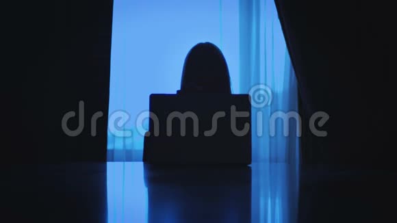 商务女性在黑暗的房间里坐在靠窗的手提电脑上工作视频的预览图