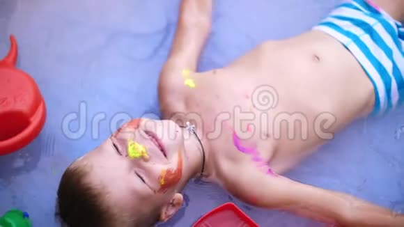 一个四岁的男孩躺在一个孩子充气游泳池里溅起水花微笑着附近的漂浮玩具从上面看视频的预览图