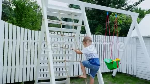 夏天在花园里孩子一个四岁的男孩爬上孩子们操场上的楼梯家庭开支视频的预览图