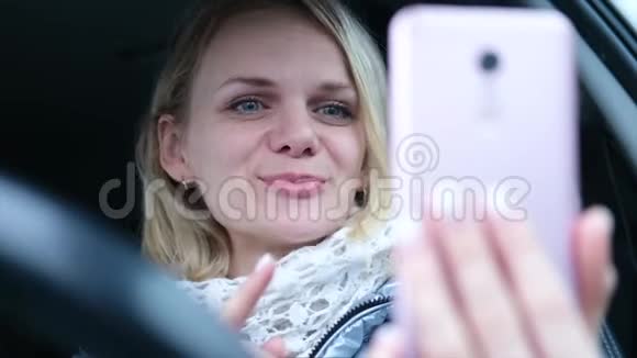 年轻女性博客写手穿着冬天的衣服坐在车里和追随者聊天现场直播寻找智能手机视频的预览图