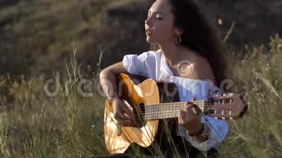 CurlyGipsy深色头发的女孩在海湾斜坡上弹吉他唱歌视频的预览图