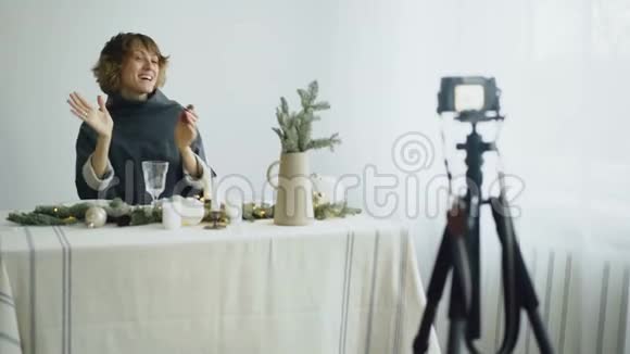 有魅力的开朗的女人坐在桌子旁在视频博客上录制关于相机桌面设计的视频视频的预览图