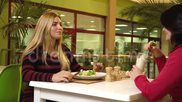 两个女人坐在健身俱乐部的咖啡馆里吃沙拉喝一杯蛋白质鸡尾酒慢动作视频的预览图