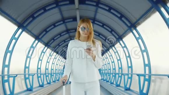 穿着白色西装的时尚商务女性穿过隧道或者从玻璃上过渡带轮子的幸运包视频的预览图