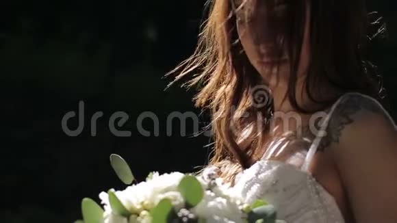 一位新娘穿着婚纱在阳光明媚的公园里开着花的肖像视频的预览图