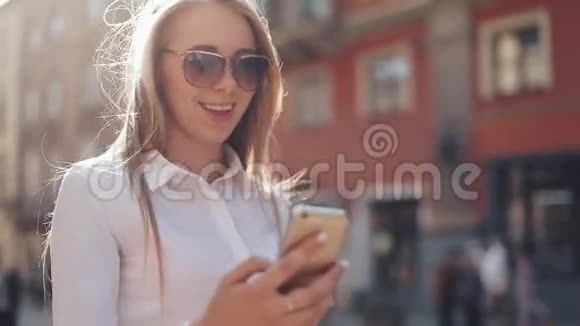 美丽的年轻商务女性穿着白色衬衫在市中心散步时使用智能手机夏季上网视频的预览图