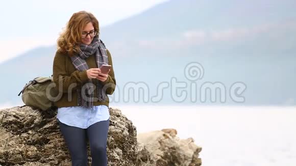 一个背着背包的女旅行者站在海边的岩石上聊天视频的预览图
