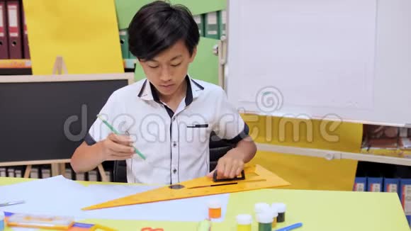 一个男孩坐在桌旁用铅笔和一把大尺子画画视频的预览图