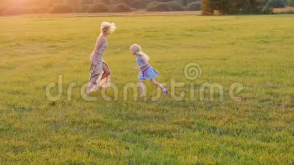 妈妈和女儿在日落时在绿色的草地上闲逛积极的生活方式视频的预览图