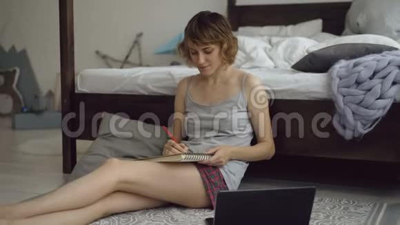 开朗的年轻女性练习用铅笔画素描用笔记本电脑坐在家里的床边视频的预览图
