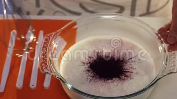 玻璃碗中深紫色和白色物质的手搅拌慢动作视频的预览图