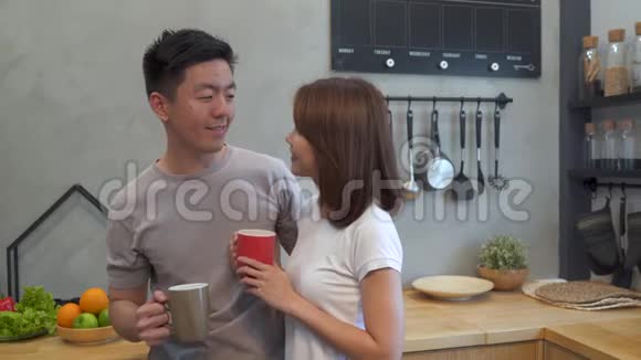 美丽快乐的亚洲夫妇正一起在厨房喝一杯咖啡男人和女人一边吃早餐一边说话视频的预览图