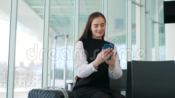 可爱的年轻旅行者女性或大学生使用手机电话在机场航站楼携带行李学习或旅行视频的预览图