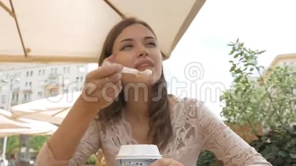 年轻漂亮的女孩在街头咖啡馆吃冰淇淋她很高兴视频的预览图