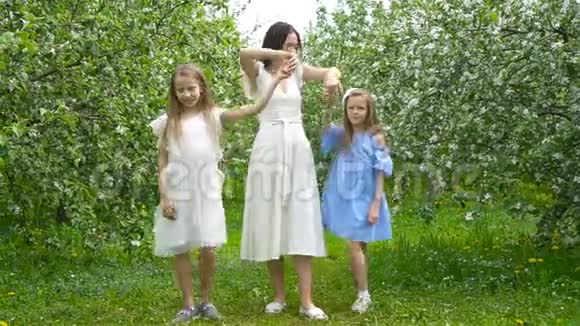 美丽的春日可爱的小女孩和年轻的母亲在盛开的花园里一起玩视频的预览图