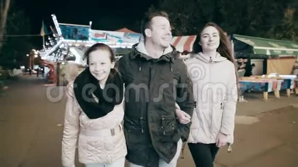 一个快乐的家庭漫步在夜城父母把女儿连接到旋转木马上的游乐园视频的预览图