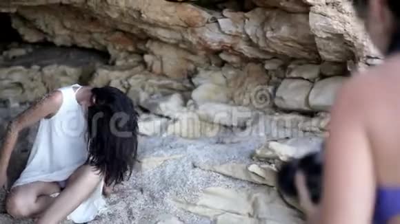 一个女孩在海边的石窟里为摄影师摆姿势希腊视频的预览图