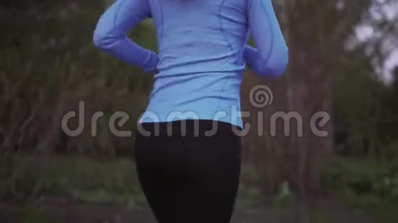慢跑一个穿蓝色运动服的年轻女孩正沿着傍晚的公园跑步后景女式双腿紧贴运动鞋视频的预览图