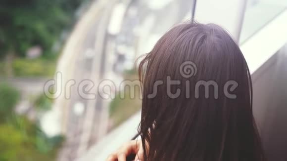 年轻的黑发美女透过窗户看城市景观与建筑道路慢动作3840x2160视频的预览图