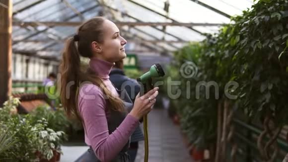年轻迷人的女园丁在温室里用花园软管均匀浇水慢镜头视频的预览图