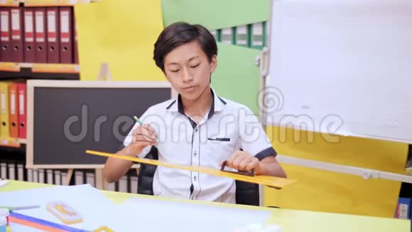 一个男孩坐在桌旁用铅笔和一把大尺子画画视频的预览图