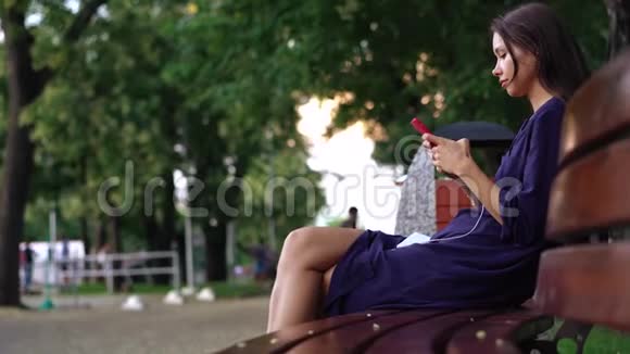 女人坐在长凳上在公园的背景上使用智能手机视频的预览图