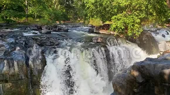 在一个美丽的阳光明媚的日子里天然瀑布穿过乡村丛林中坚硬的棕色岩石视频的预览图
