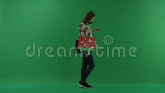 女孩站在她的左边手里拿着袋子在绿色屏幕上用手机聊天视频的预览图