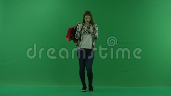 女孩站在肩上背着包在绿色屏幕上的手机帮助下聊天视频的预览图