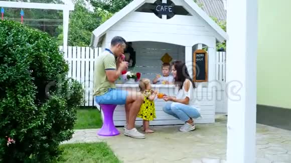 夏天在花园里父母和孩子们一起玩一个女孩和一个男孩在咖啡馆里在一个孩子游戏屋里请客视频的预览图