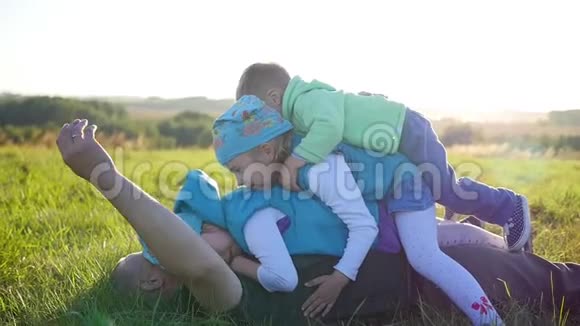 快乐的年轻父亲和他的孩子躺在公园的草坪上三个快乐的孩子和他们的父亲一起玩儿童视频的预览图