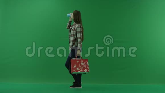 女孩站在她的左边拿着袋子在绿色的屏幕上喝着杯子里的东西视频的预览图