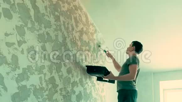 画家用滚筒画墙的背面视图在白色粪堆中的画家头盔和手套的背面画一堵墙视频的预览图