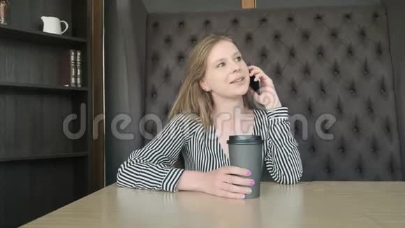 年轻漂亮的女孩在咖啡馆里通过智能手机打电话她下班前喝早咖啡概念早餐放松视频的预览图