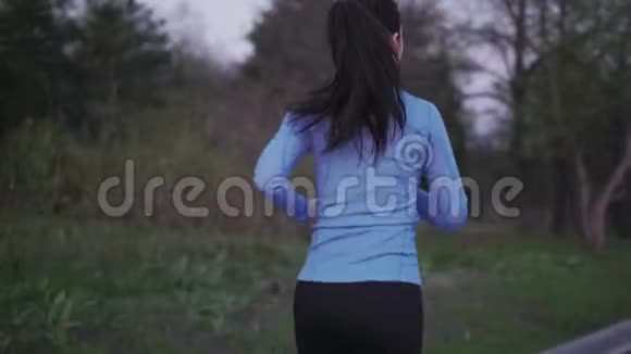 女孩在户外训练慢跑一个穿蓝色运动服的年轻女孩正沿着傍晚的公园跑步后景女性视频的预览图