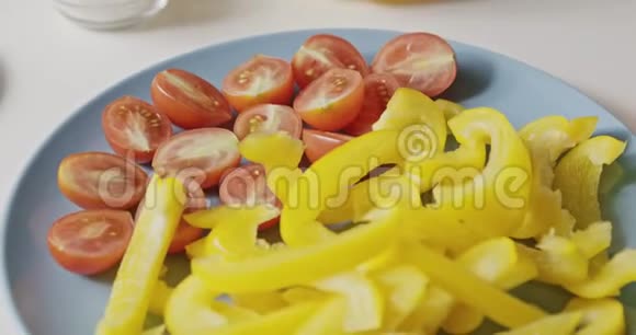 将成熟的红西红柿和黄色辣椒切成薄片放在白色桌子上的蓝色陶瓷盘子上上面有有机天然成分视频的预览图