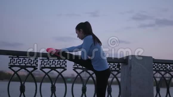 运动员把脚放在堤岸上的栅栏上做伸展运动视频的预览图