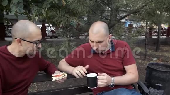 两个秃头正坐在公园里吃三明治和炸薯条喝咖啡说话美味的食物视频的预览图