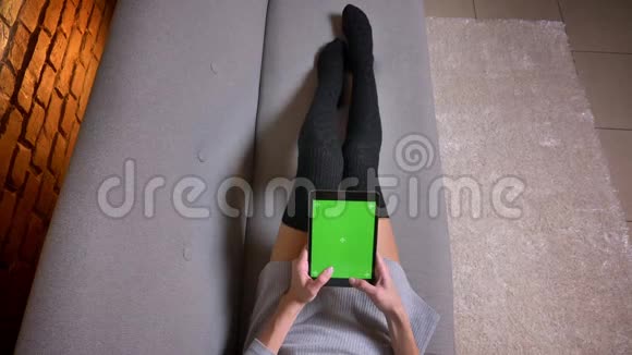 室内沙发上穿着可爱袜子的女腿特写镜头女人用绿色屏幕在平板电脑上打字视频的预览图