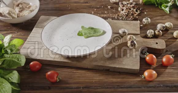 一个女人用手把绿色的菠菜叶扔在白色的陶瓷盘子上背景是鹌鹑蛋鸡柳视频的预览图