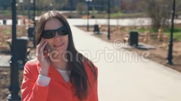 年轻的黑发女人戴着太阳镜在春天公园打电话视频的预览图