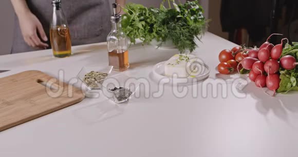 穿围裙的女人准备做蔬菜沙拉奶酪物种桌子上西红柿萝卜辣椒奶酪视频的预览图